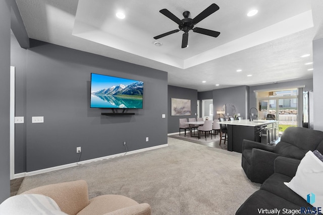 living room featuring a raised ceiling, baseboards, light colored carpet, and recessed lighting