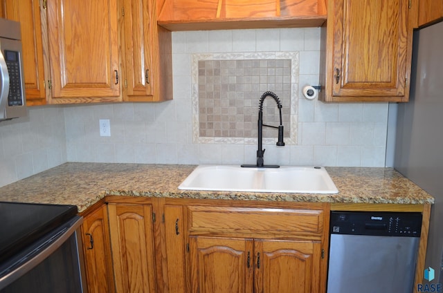 kitchen featuring brown cabinets, light countertops, a sink, tasteful backsplash, and appliances with stainless steel finishes