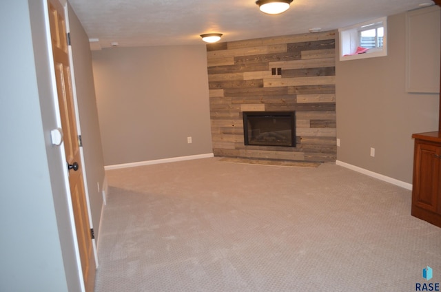 unfurnished living room with baseboards, wooden walls, a stone fireplace, and carpet flooring