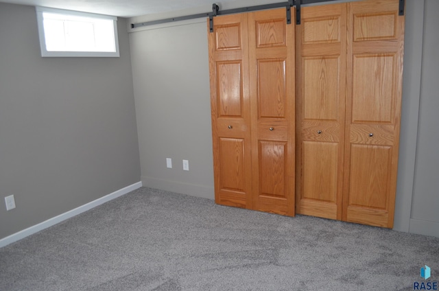unfurnished bedroom featuring a barn door, baseboards, and carpet