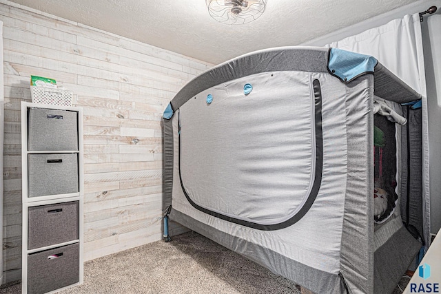 bedroom with wooden walls, carpet, and a textured ceiling