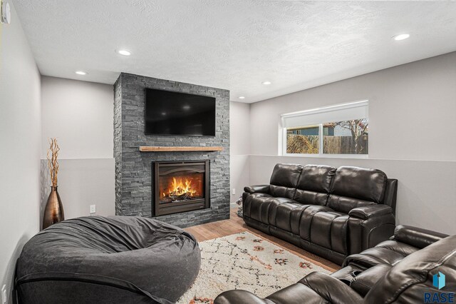 living area featuring recessed lighting, wood finished floors, a textured ceiling, and a stone fireplace