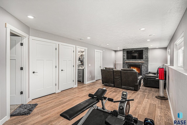workout room featuring baseboards, a large fireplace, light wood finished floors, and recessed lighting