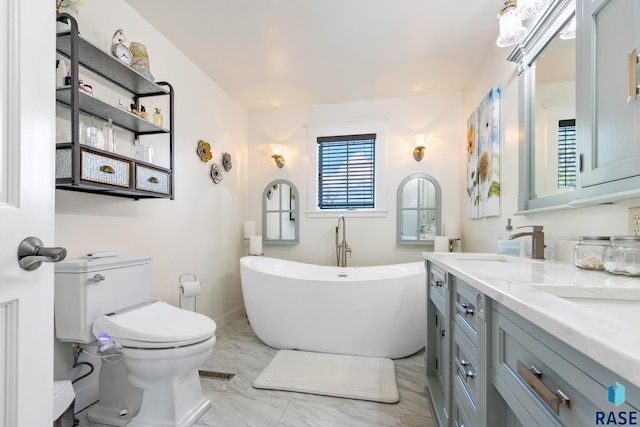 full bath with marble finish floor, a freestanding bath, double vanity, toilet, and a sink