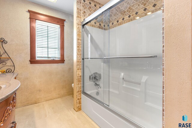 full bathroom with bath / shower combo with glass door, toilet, wood finished floors, a textured wall, and vanity