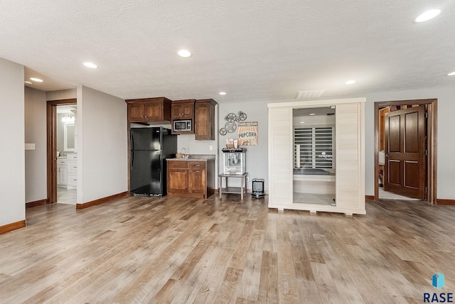 kitchen featuring stainless steel microwave, freestanding refrigerator, light wood-type flooring, and baseboards