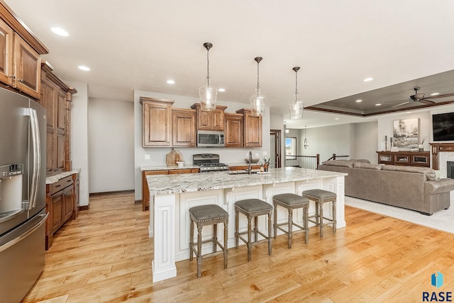 kitchen with a sink, brown cabinetry, open floor plan, light wood finished floors, and appliances with stainless steel finishes