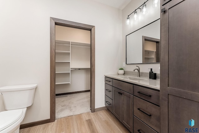 bathroom featuring baseboards, wood finished floors, toilet, and vanity