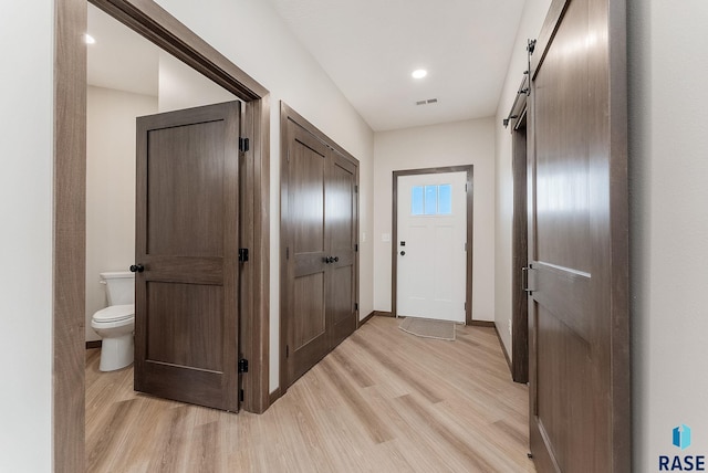 hall with visible vents, baseboards, a barn door, and light wood-style floors