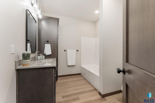 bathroom with bathing tub / shower combination, vanity, baseboards, and wood finished floors