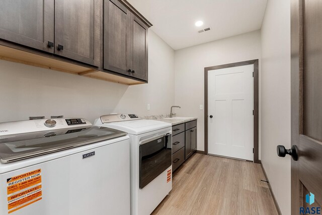 laundry area featuring visible vents, a sink, light wood-type flooring, independent washer and dryer, and cabinet space
