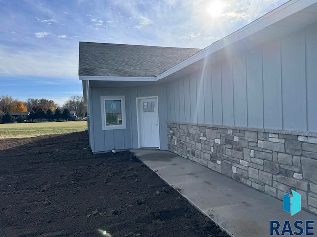 view of exterior entry featuring board and batten siding, stone siding, and a shingled roof