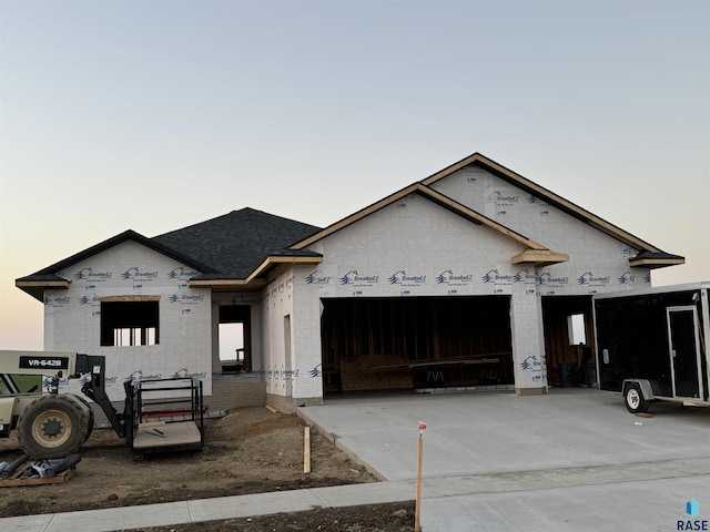 unfinished property featuring an attached garage, a shingled roof, and driveway