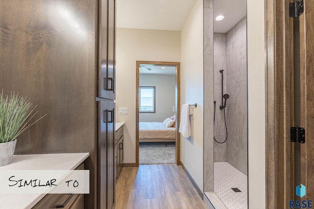 bathroom with baseboards, wood finished floors, vanity, and tiled shower