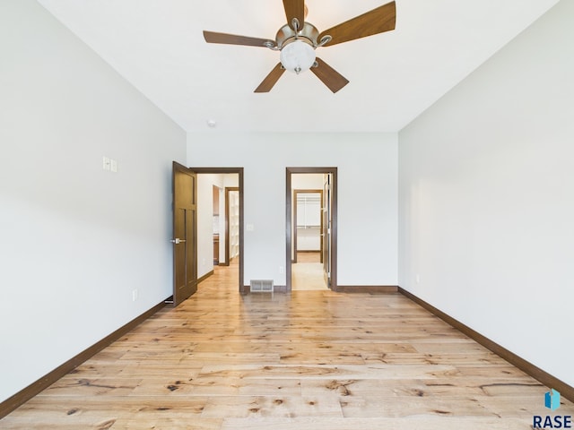 unfurnished bedroom featuring a spacious closet, light wood-style floors, ceiling fan, baseboards, and visible vents