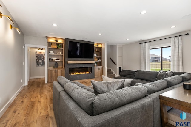 living room with light wood-style flooring, a glass covered fireplace, baseboards, recessed lighting, and stairway