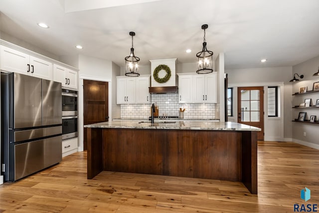 kitchen with a sink, light wood-style floors, stainless steel appliances, backsplash, and white cabinetry