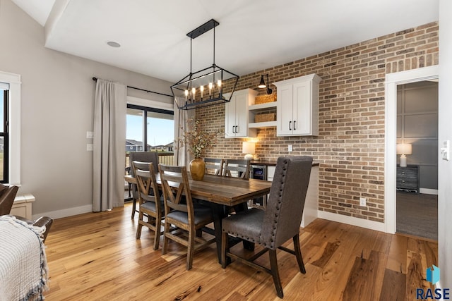 dining room with light wood-type flooring, brick wall, and an inviting chandelier