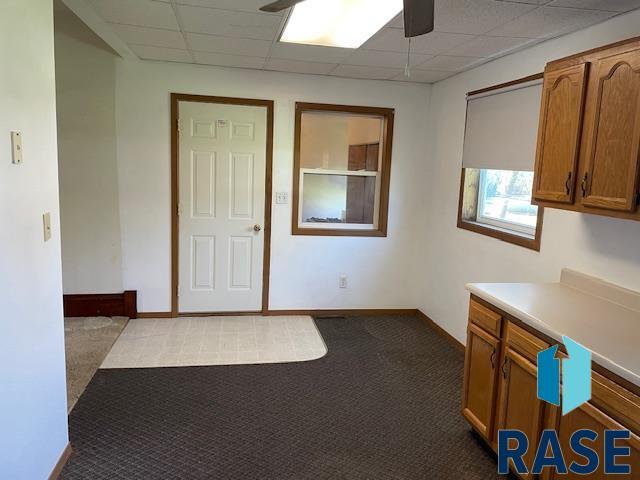 1131 Williams St, Larchwood, IA 51241 - interior space with dark colored carpet, a drop ceiling, baseboards, and ceiling fan
