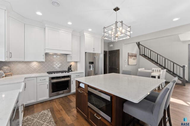 912 Torrey Pine Ln, Sioux Falls, SD 57110 - kitchen featuring a notable chandelier, stainless steel appliances, a breakfast bar, decorative backsplash, and dark wood-style flooring