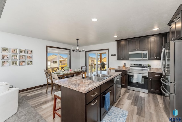 kitchen featuring stainless steel appliances, a sink, light wood-type flooring, a kitchen island with sink, and a chandelier