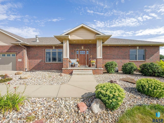 view of front of house with an attached garage, brick siding, a shingled roof, and covered porch