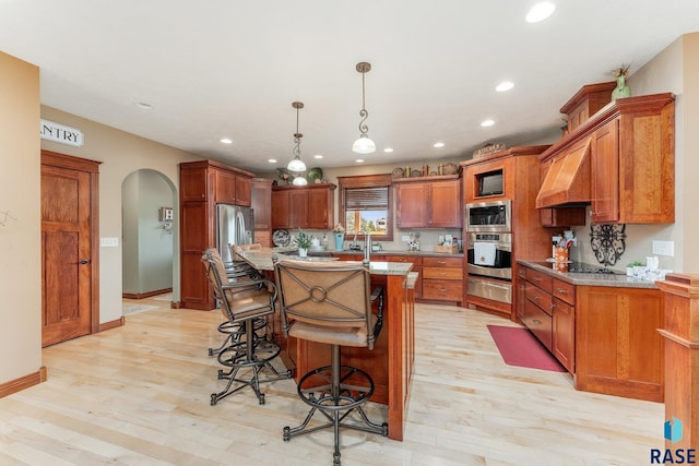 kitchen with stainless steel appliances, a breakfast bar, arched walkways, premium range hood, and light wood-style flooring