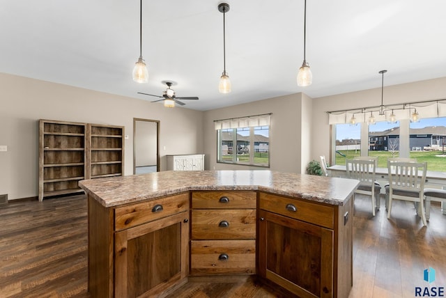 3508 E Prairie Wind St, Sioux Falls, SD 57108 - kitchen featuring a ceiling fan, brown cabinets, decorative light fixtures, dark wood-style floors, and a kitchen island