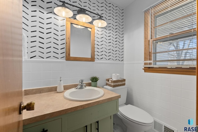 bathroom featuring a wainscoted wall, visible vents, toilet, vanity, and tile walls
