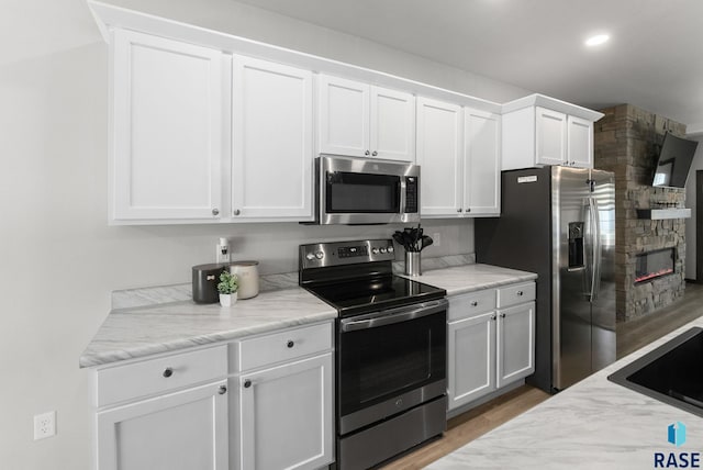 kitchen with recessed lighting, stainless steel appliances, a fireplace, light wood-style flooring, and white cabinetry