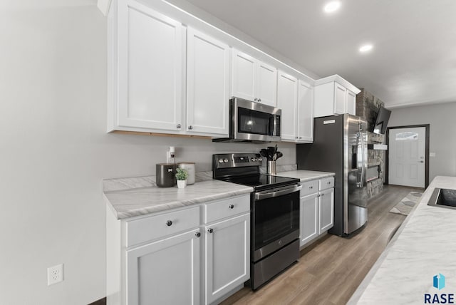 kitchen with white cabinets, light wood-type flooring, recessed lighting, light countertops, and appliances with stainless steel finishes