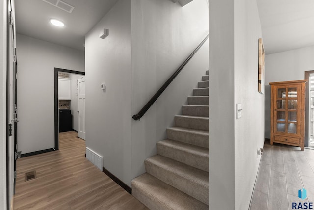 staircase featuring baseboards, wood finished floors, and visible vents