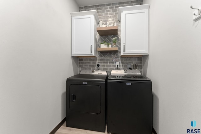 washroom featuring washing machine and dryer, light wood-style floors, and cabinet space