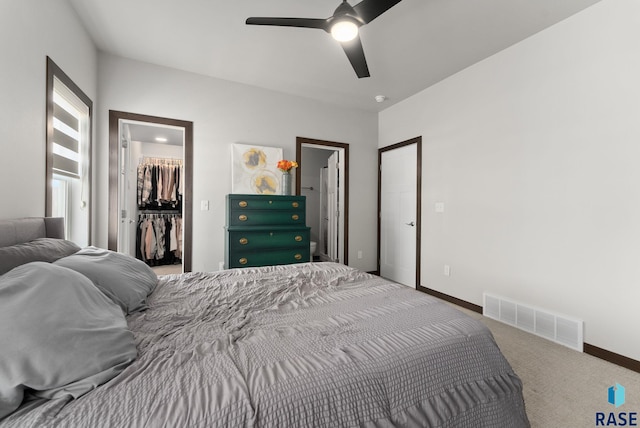 carpeted bedroom with a closet, a walk in closet, ceiling fan, baseboards, and visible vents