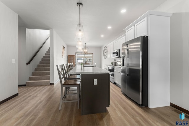 kitchen with a sink, stainless steel appliances, a center island with sink, baseboards, and white cabinetry