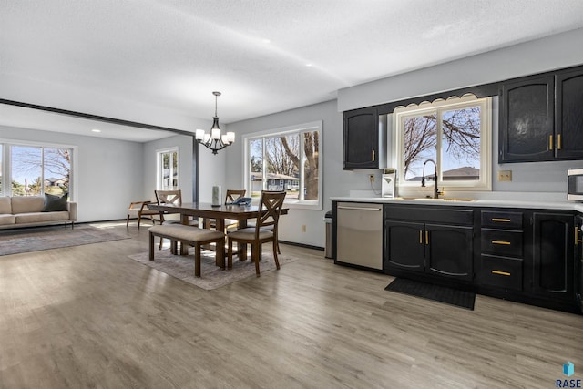 kitchen with stainless steel appliances, an inviting chandelier, light countertops, a sink, and light wood-type flooring