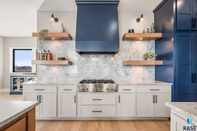 kitchen featuring open shelves, stainless steel gas cooktop, custom range hood, light wood-style flooring, and backsplash