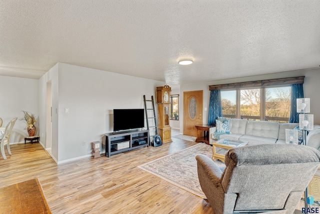living room with light wood-style flooring, a textured ceiling, and baseboards