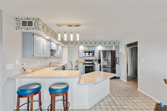 kitchen featuring a breakfast bar, a peninsula, stainless steel appliances, light countertops, and baseboards