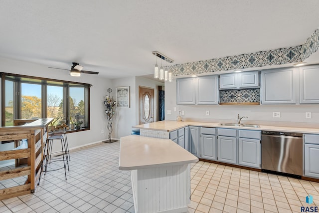 kitchen featuring light countertops, dishwasher, a sink, gray cabinetry, and a peninsula