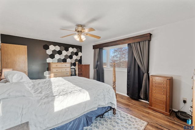 bedroom with an accent wall, wood finished floors, a ceiling fan, and baseboards