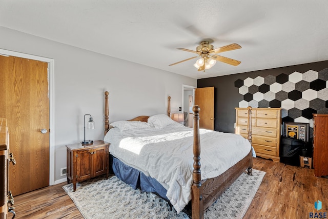 bedroom featuring an accent wall, light wood-style floors, and ceiling fan