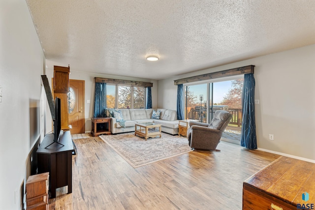 living area featuring light wood-style floors, a textured ceiling, and baseboards