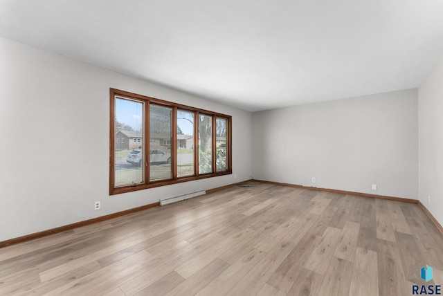 unfurnished room featuring baseboards, light wood-type flooring, and baseboard heating