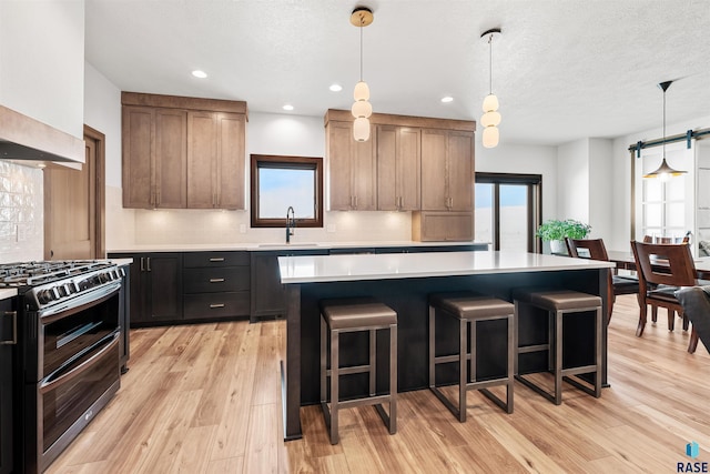 kitchen featuring a kitchen breakfast bar, light countertops, a sink, decorative backsplash, and range with two ovens
