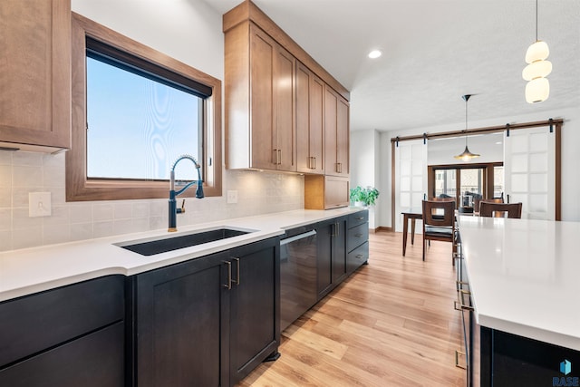 kitchen with a barn door, light countertops, backsplash, stainless steel dishwasher, and a sink