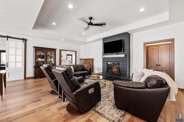living room featuring a ceiling fan, light wood finished floors, a raised ceiling, baseboards, and a brick fireplace