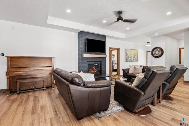 living room with a fireplace, a ceiling fan, a tray ceiling, and light wood-style floors