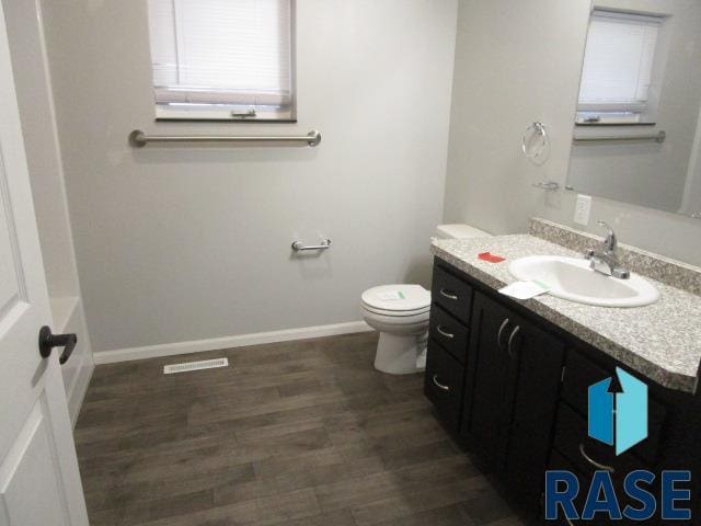 bathroom with wood finished floors, vanity, baseboards, toilet, and visible vents