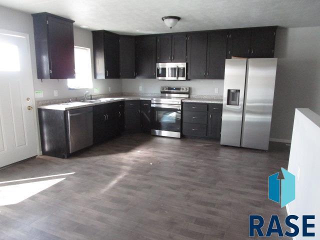 kitchen featuring dark cabinets, stainless steel appliances, dark wood-style floors, and light countertops